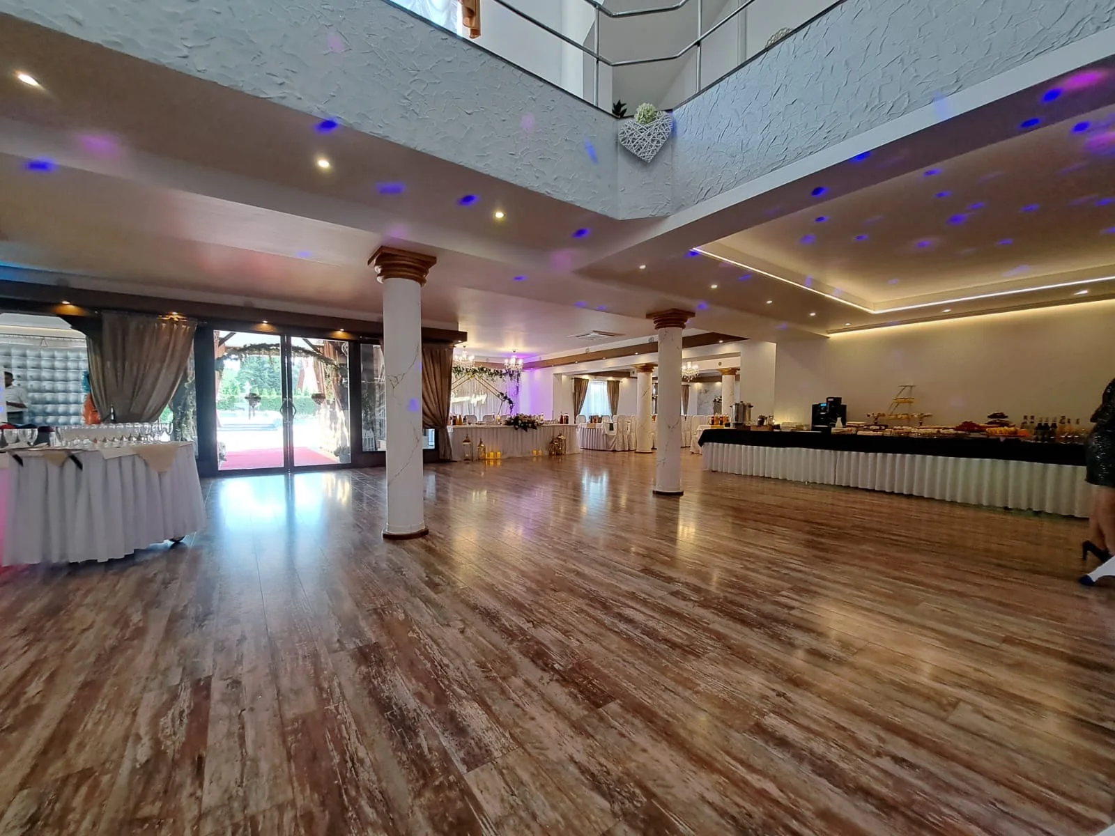 Przestronna sala z parkietem, antresolą i stołami przy ścianach